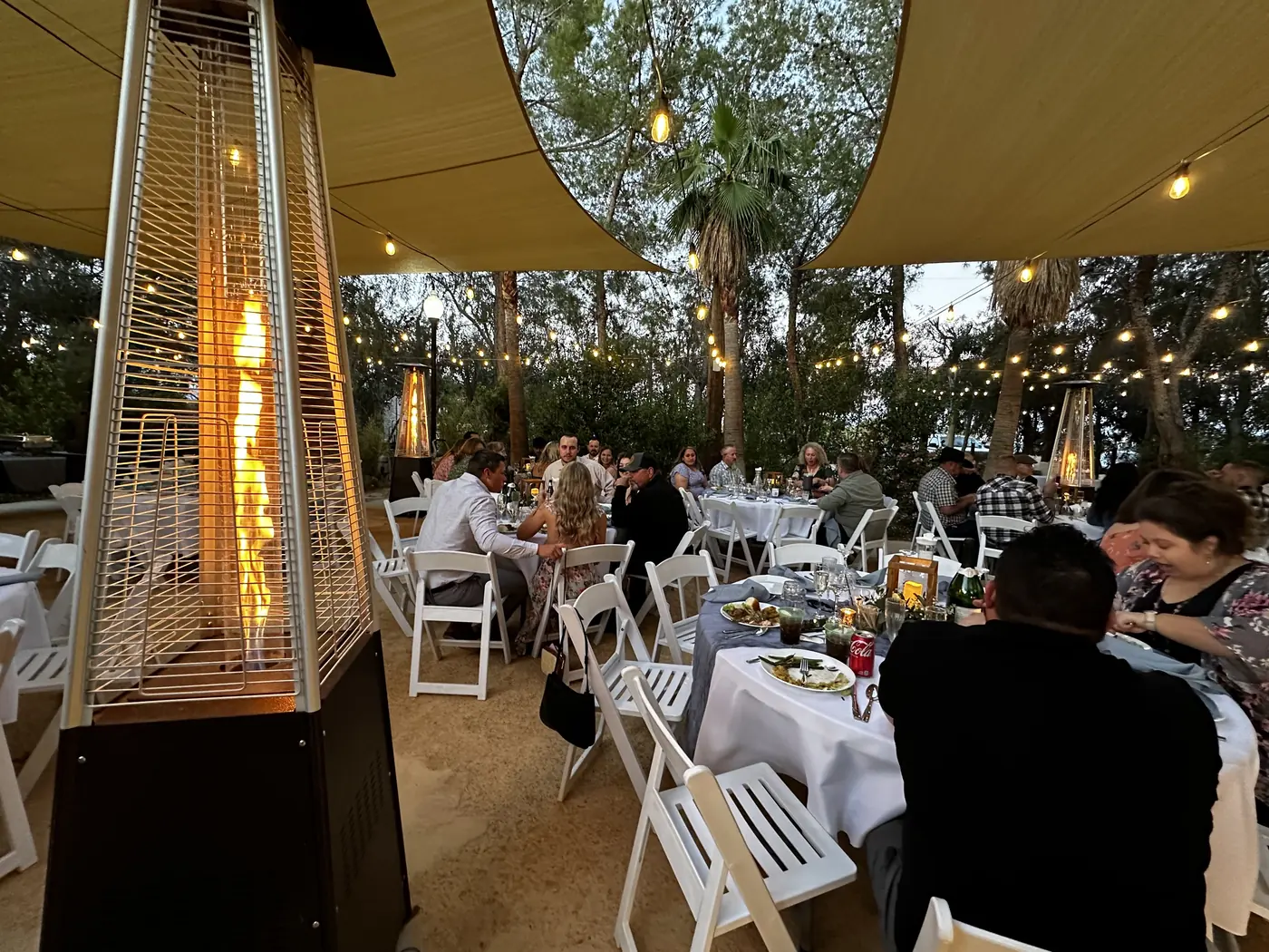 Guests dining under the sail shades and tower heaters at dusk at The Garden